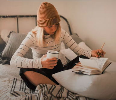 Mädchen auf einem Bett, die etwas in ein Buch schreibt. Mit Mütze auf dem Kopf.
