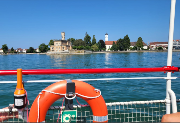 foto vom schiff aus ans ufer, wo alte, hübsche bauten unter bäumen stehen